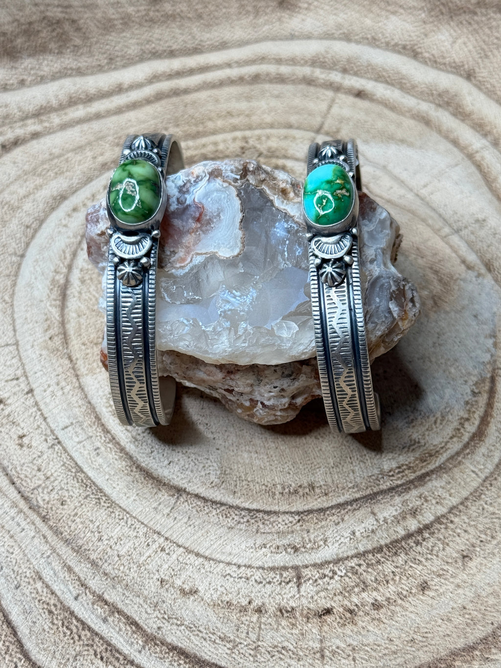 Two silver bracelets with green stones on a textured stone surface