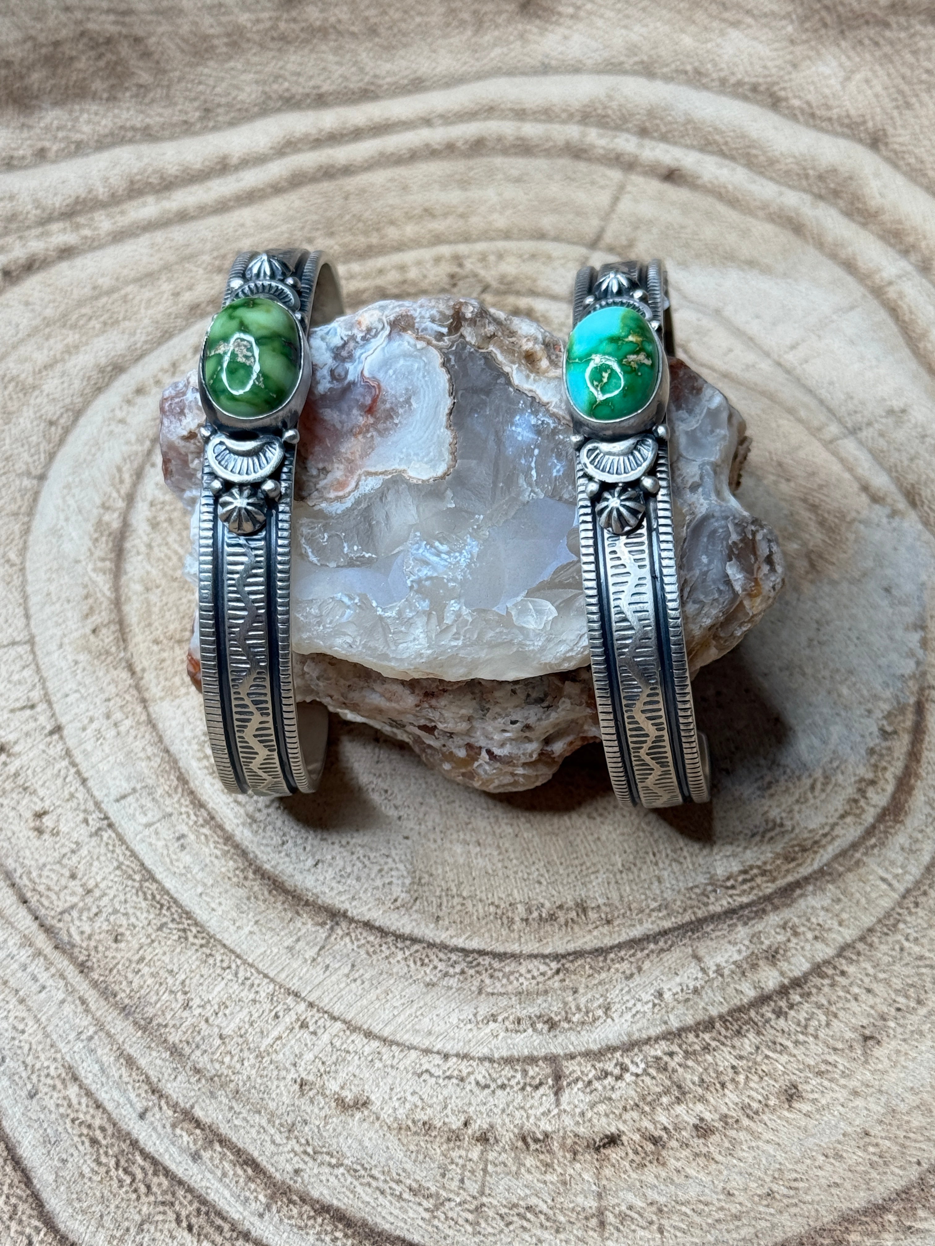 Two silver bracelets with green stones on a textured stone surface