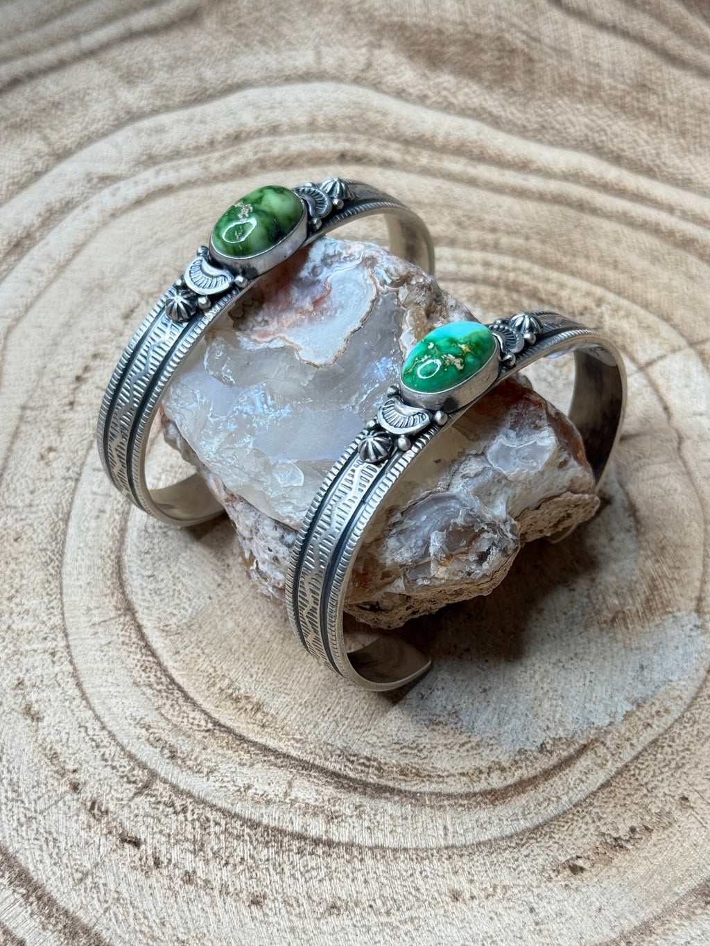 Silver bracelet with green stones on a crystal and sand background