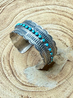 Silver cuff bracelet with turquoise stones on a textured beige surface