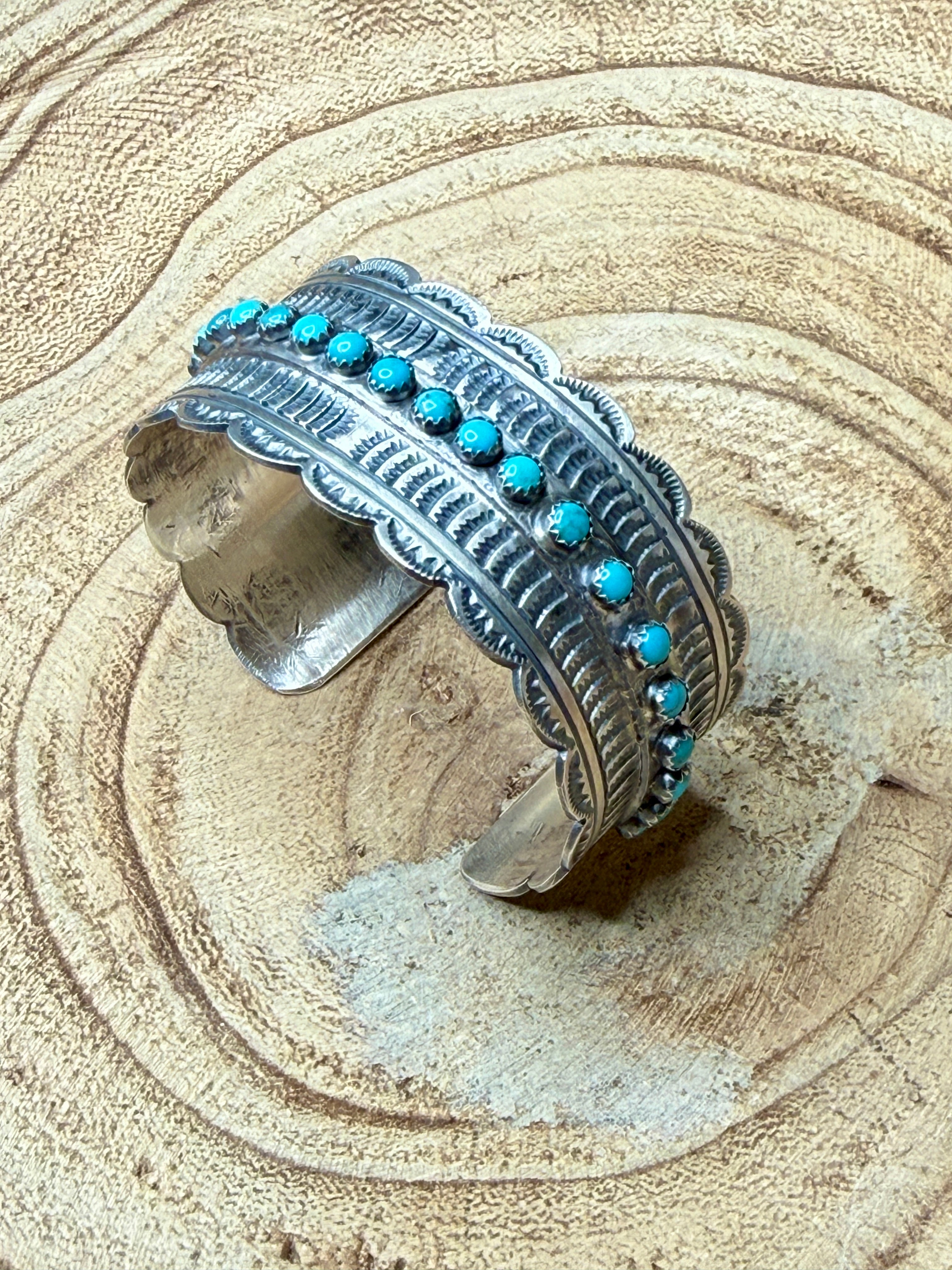 Silver cuff bracelet with turquoise stones on a textured beige surface