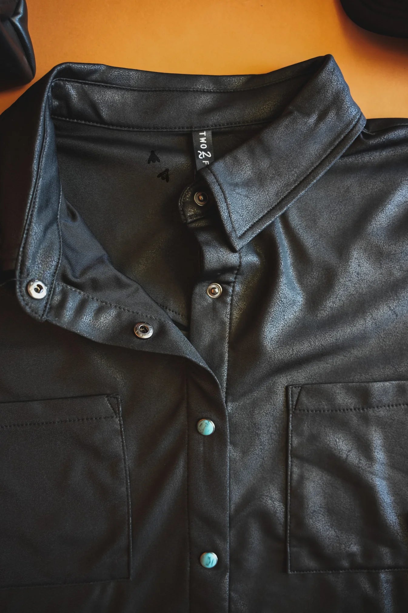 Close-up of a black leather jacket with buttons and pockets.