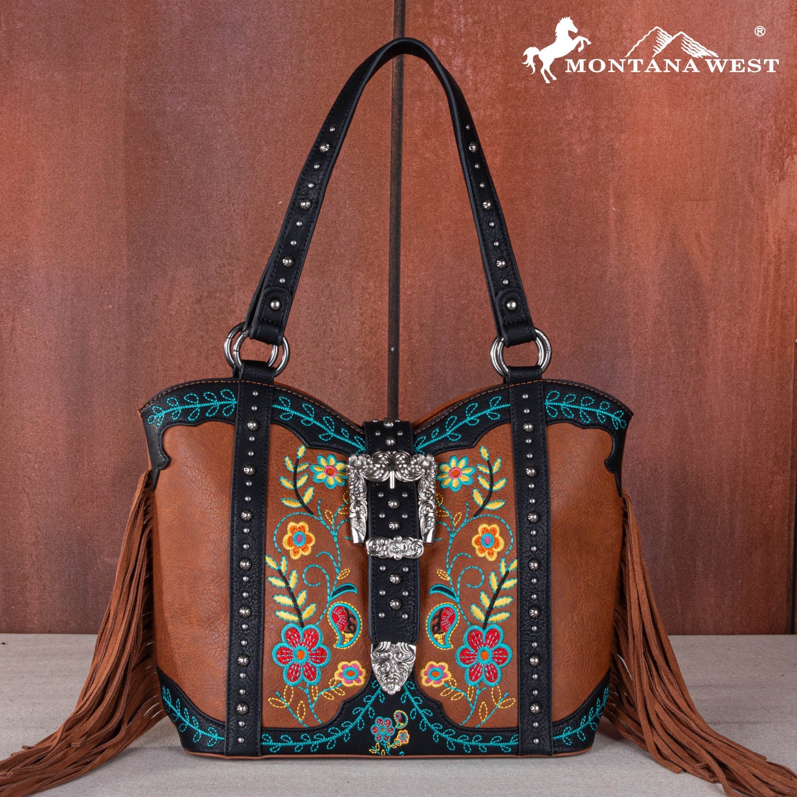 Brown leather handbag with floral embroidery and fringes on a wooden background, featuring the Montana West logo.