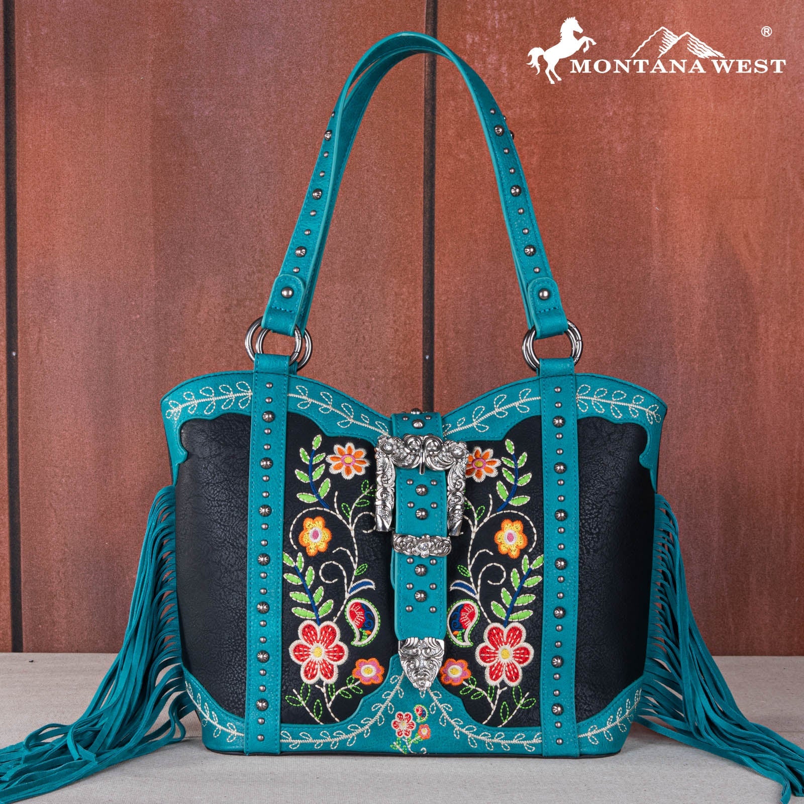 Teal handbag with floral embroidery and fringe on a wooden background, featuring the Montana West logo.
