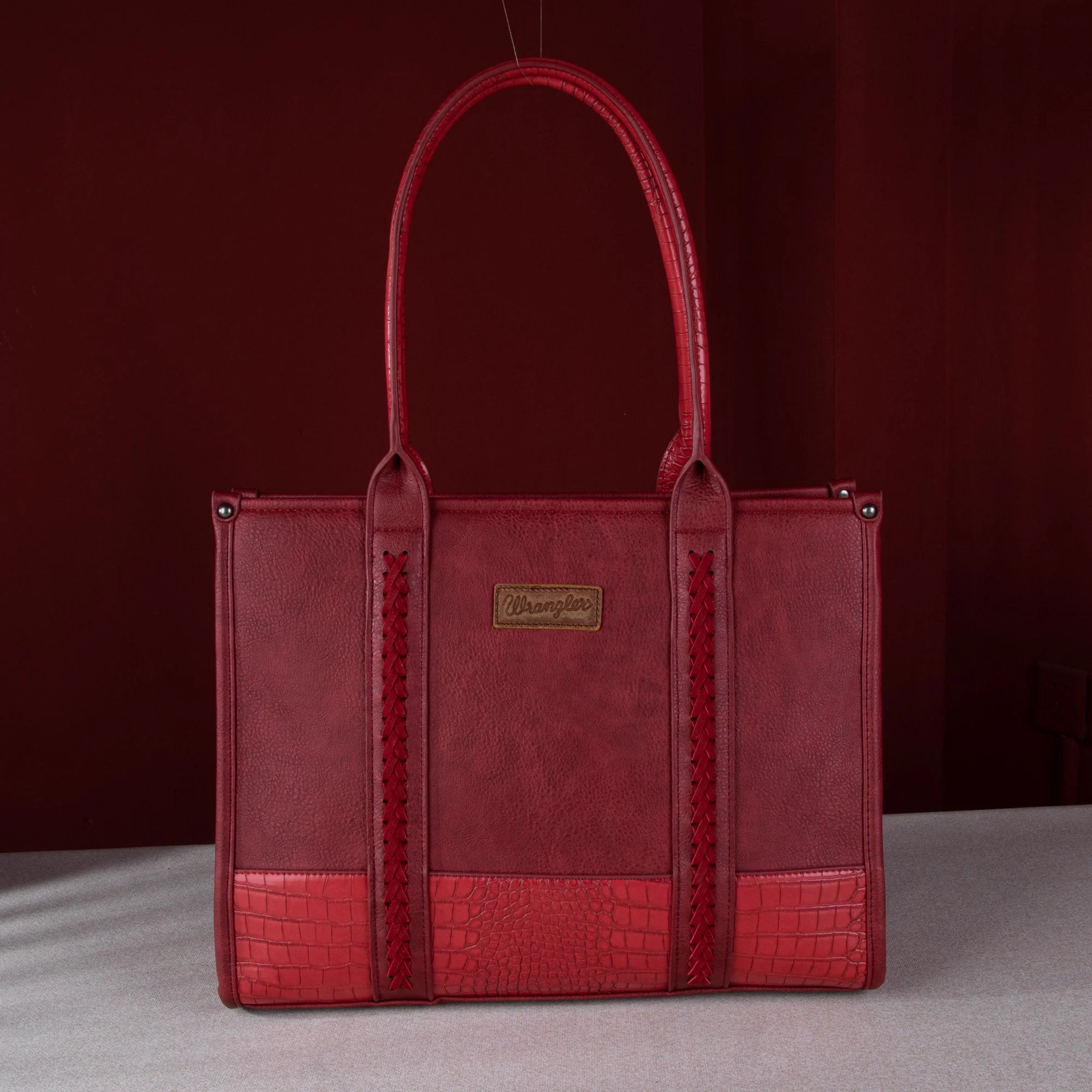 Red handbag with a textured pattern on a gray surface and dark red background