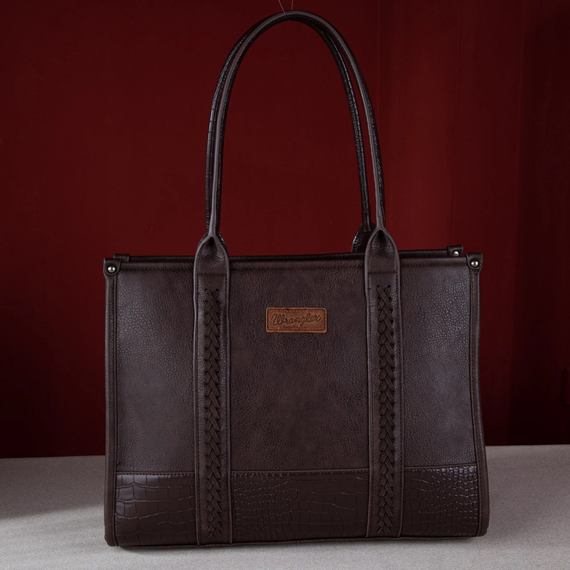 Brown leather tote bag with braided handles on a red background