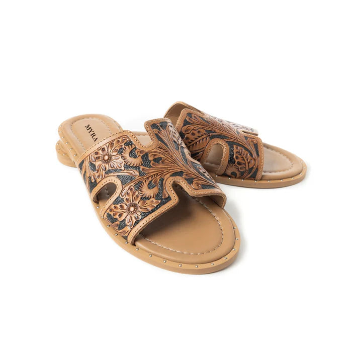 A brown leather slip-on sandal with intricate tooled floral designs and an open toe.