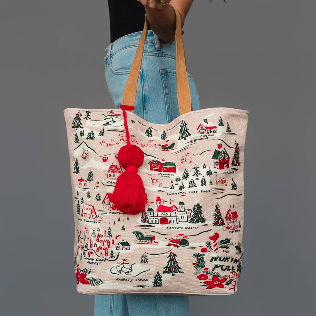 Tote bag with Christmas-themed design and red pom-pom held by a person against a gray background