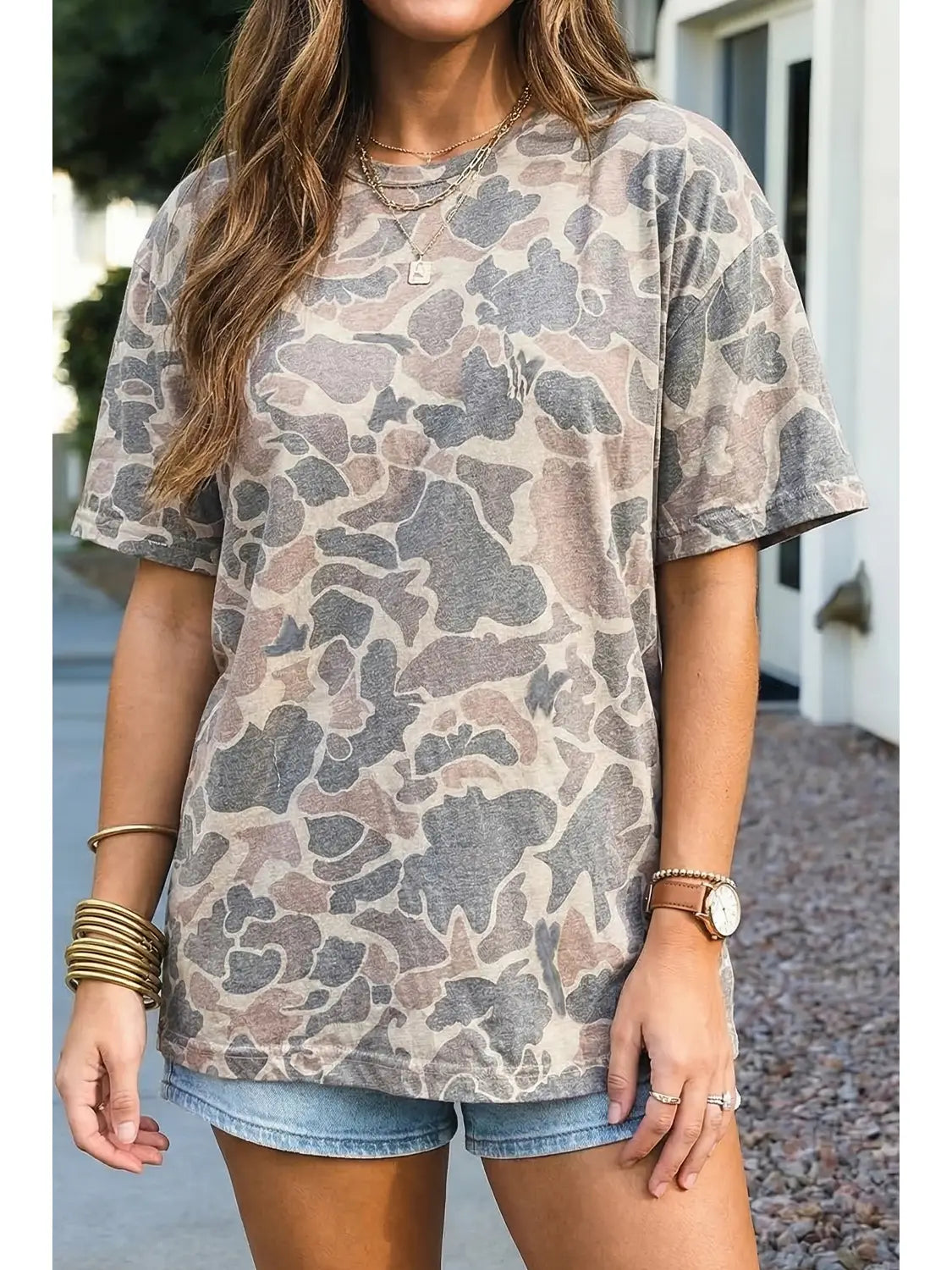 A woman wearing an oversized short-sleeve t-shirt with a muted camouflage pattern in beige, gray, and brown, paired with denim shorts.