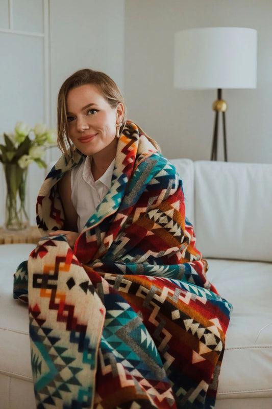 Woman wrapped in a colorful patterned blanket sitting on a couch.