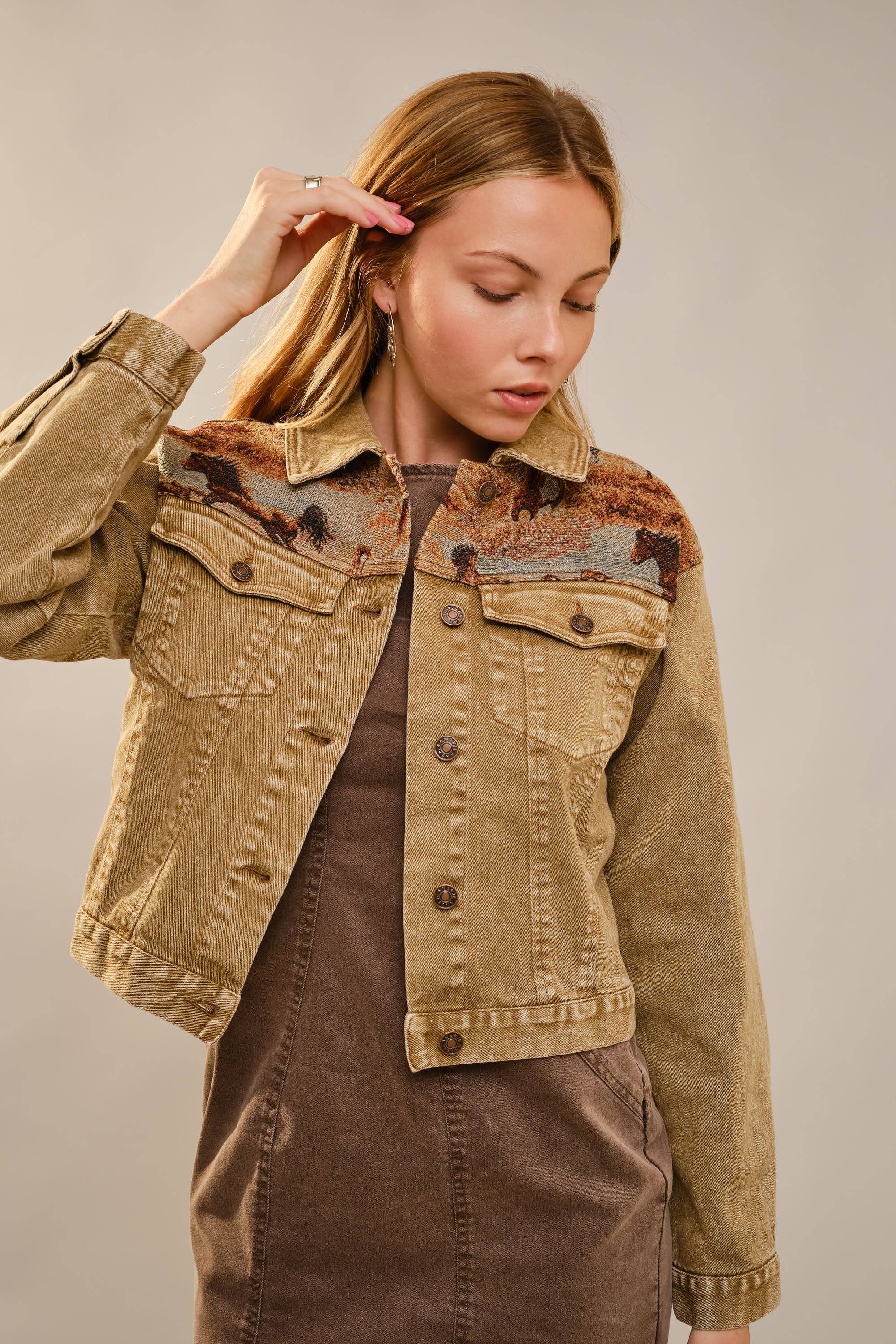 Woman wearing a brown denim jacket against a plain background