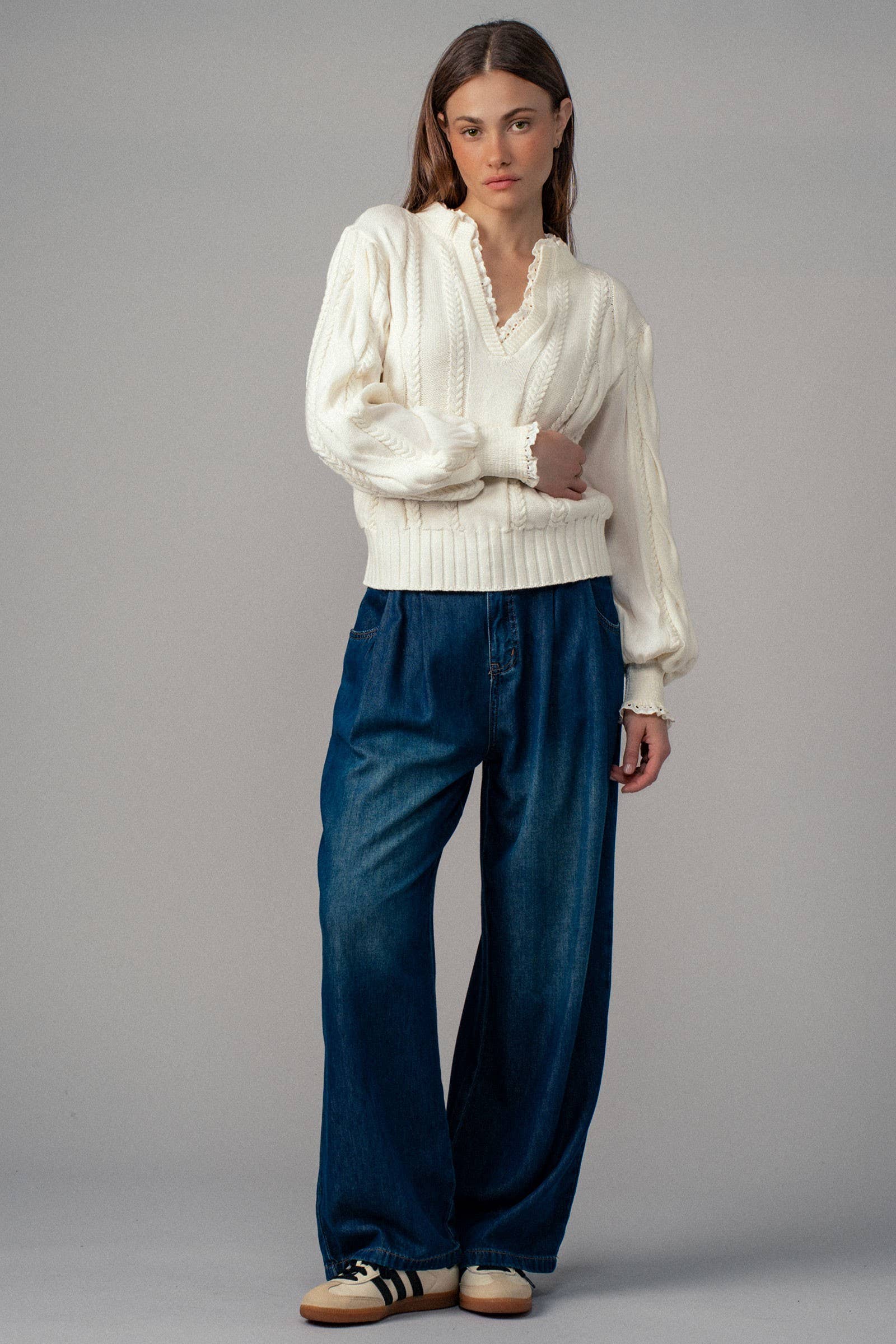 Woman wearing a white sweater and blue jeans against a gray background