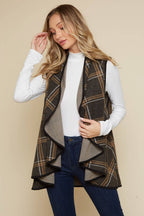 Woman wearing a plaid vest over a white shirt and blue jeans on a beige background