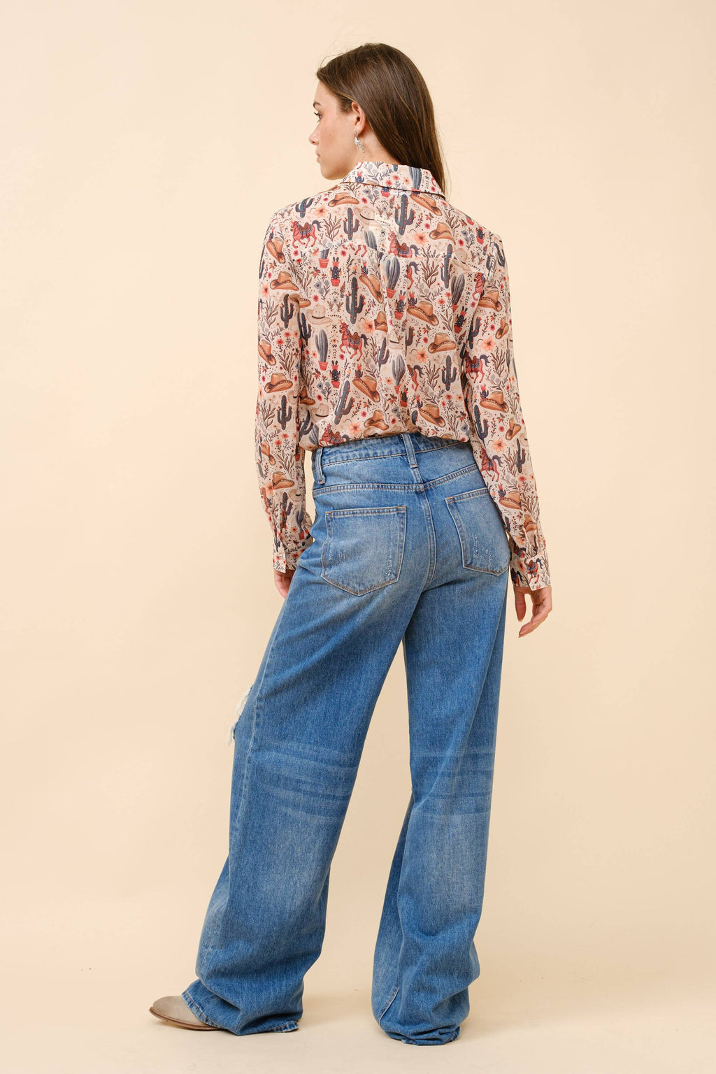 Woman wearing a patterned blouse and blue jeans on a beige background
