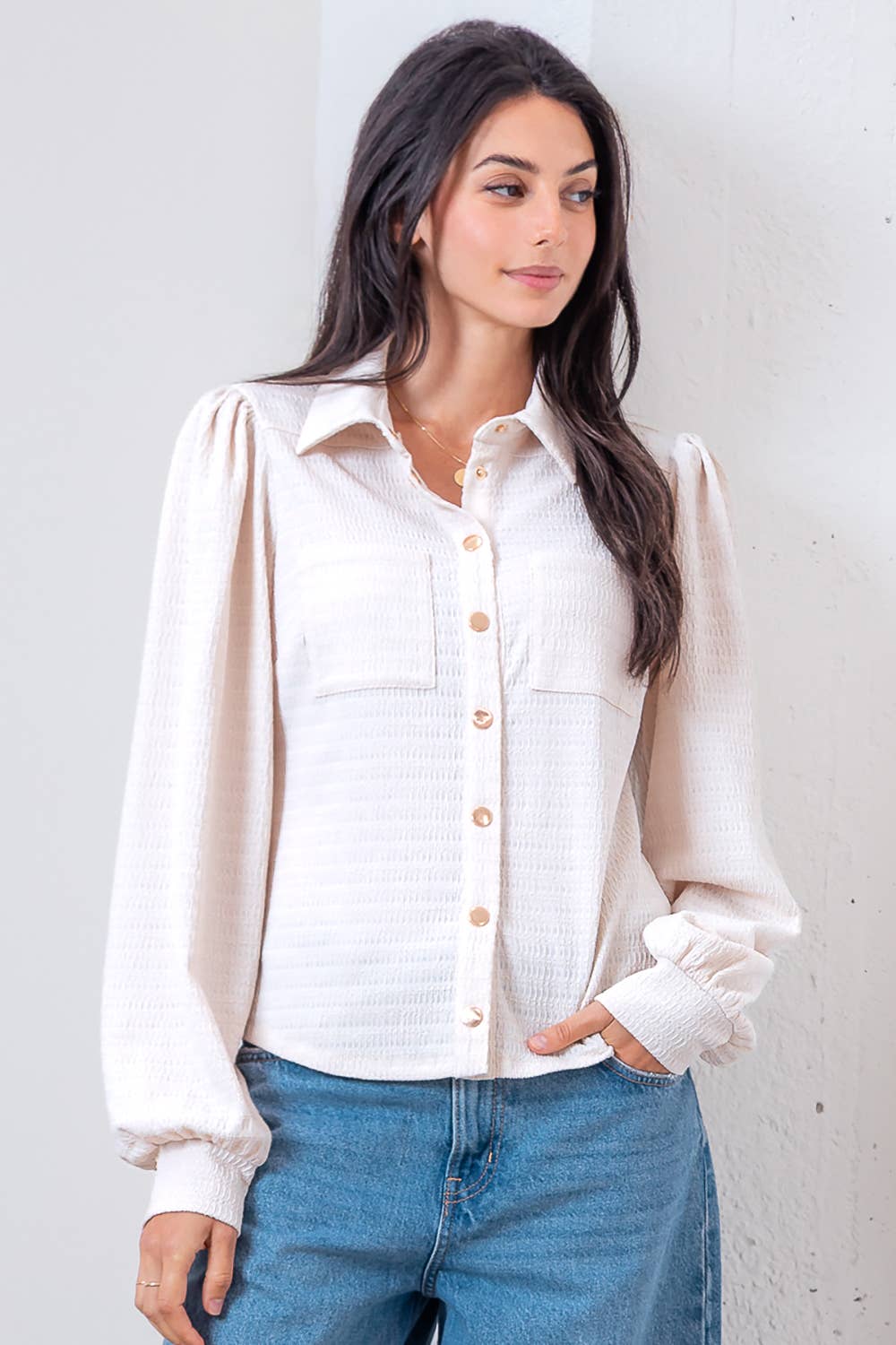 Woman wearing a white blouse with long sleeves and blue jeans against a plain background