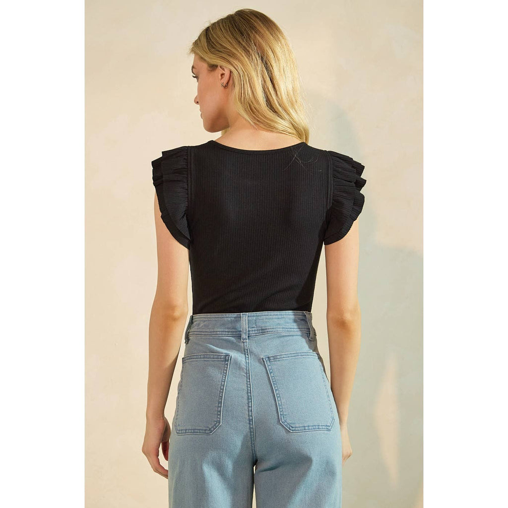 Woman wearing a black top with ruffled sleeves and light blue jeans against a neutral background