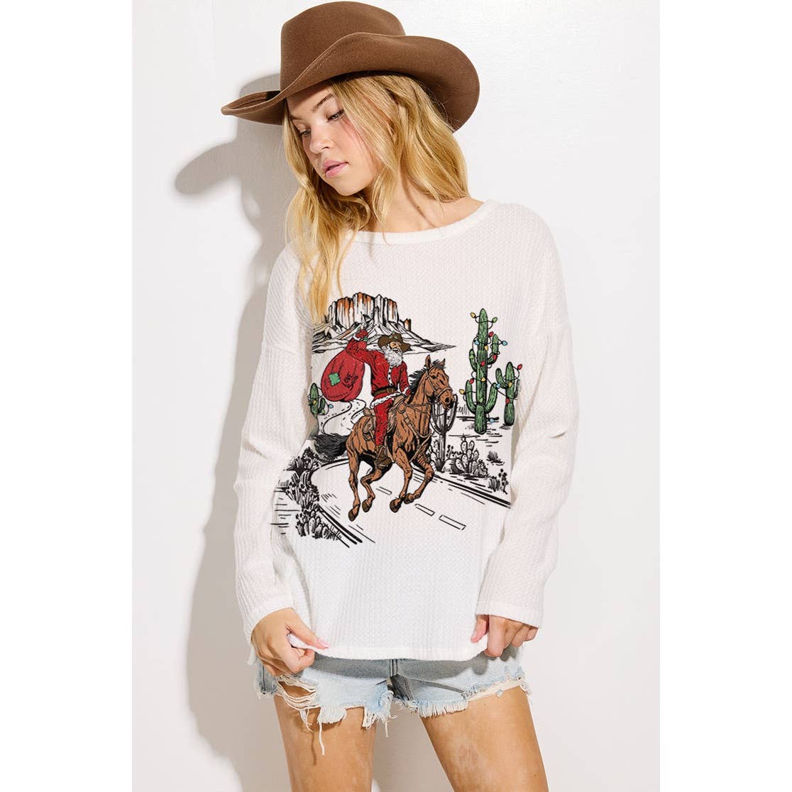 Woman wearing a white sweatshirt with a graphic design of a cowboy on a horse, cactus, and landscape.
