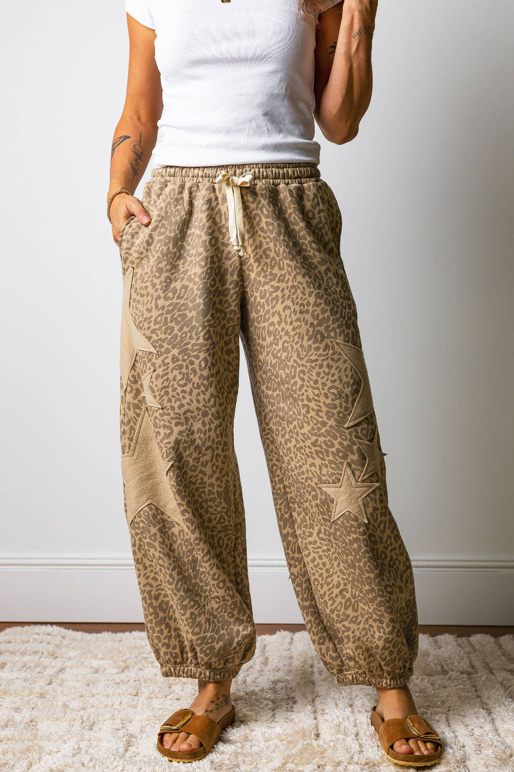 Person wearing beige patterned pants and a white top on a plain background
