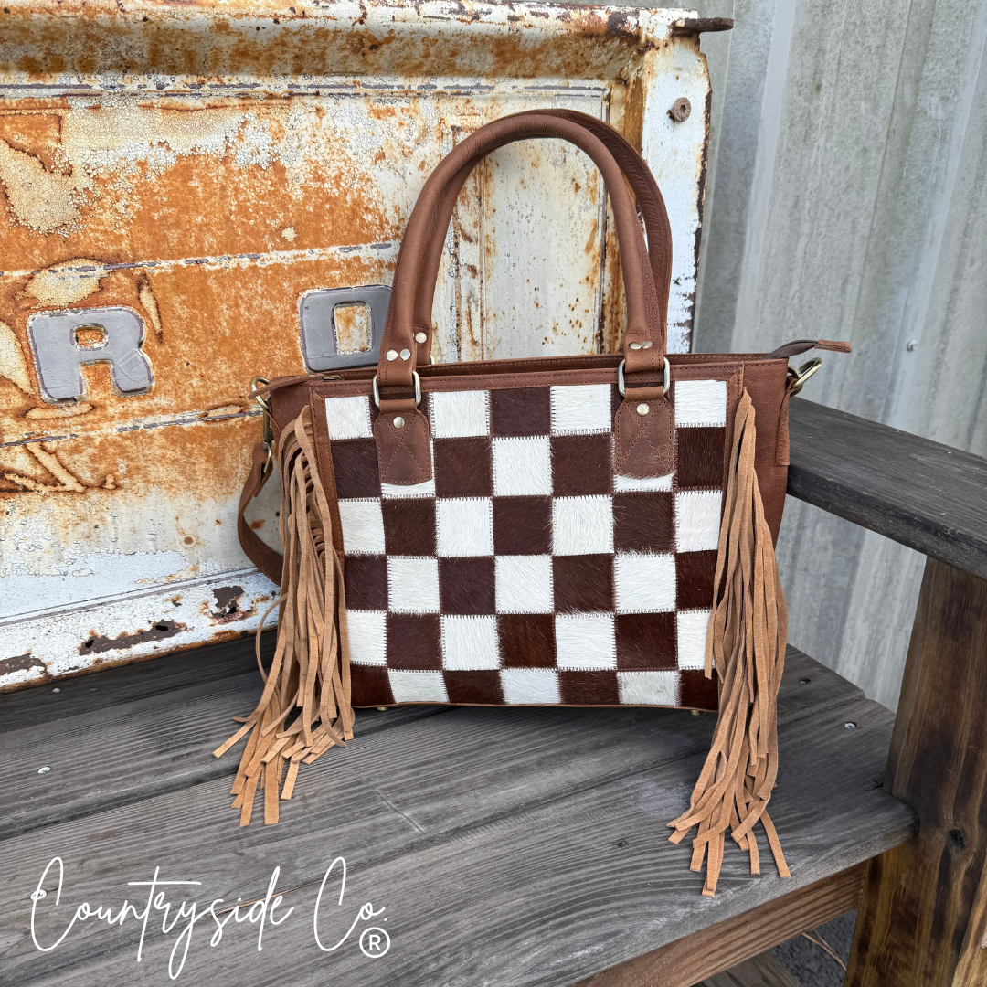 Checkered handbag with fringes on a wooden surface, featuring the 'Countryside Co' brand.