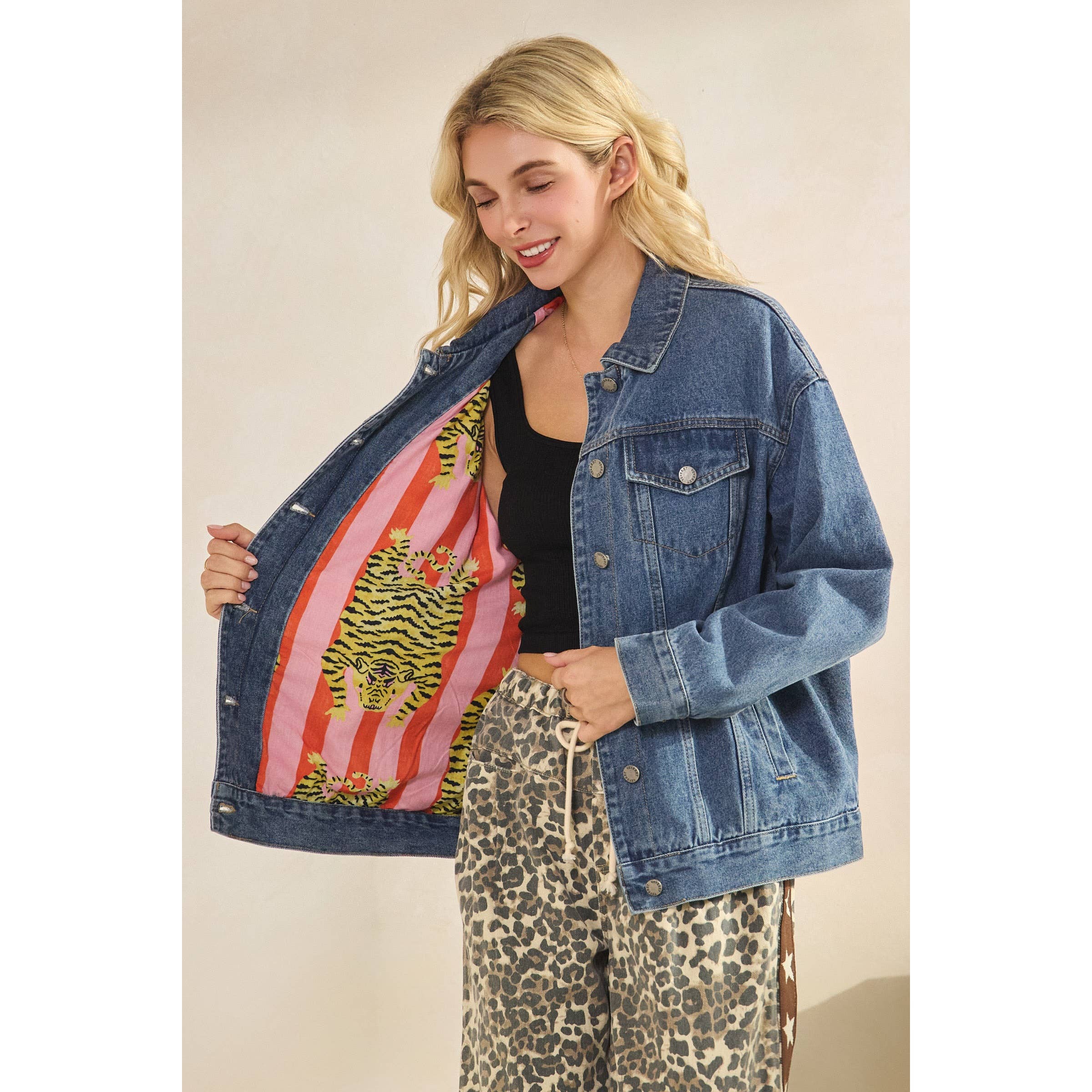 Woman wearing a blue denim jacket and leopard print pants against a beige background with pink stripe interior