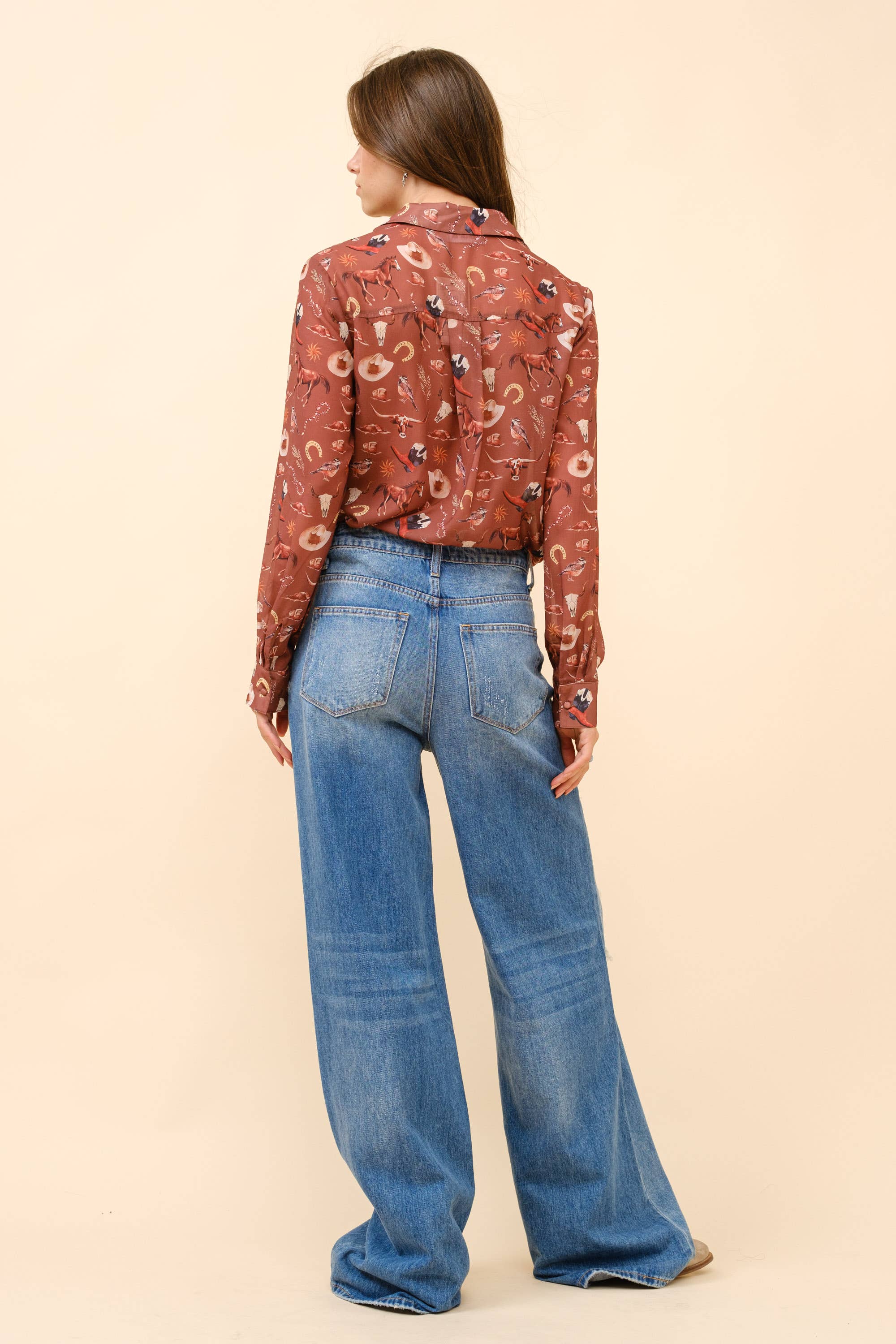 Woman wearing a patterned blouse and blue jeans on a beige background