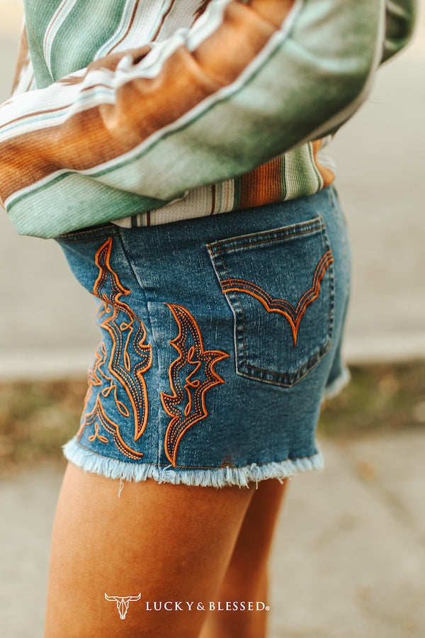 Close-up of denim shorts with intricate embroidery and a blurred background
